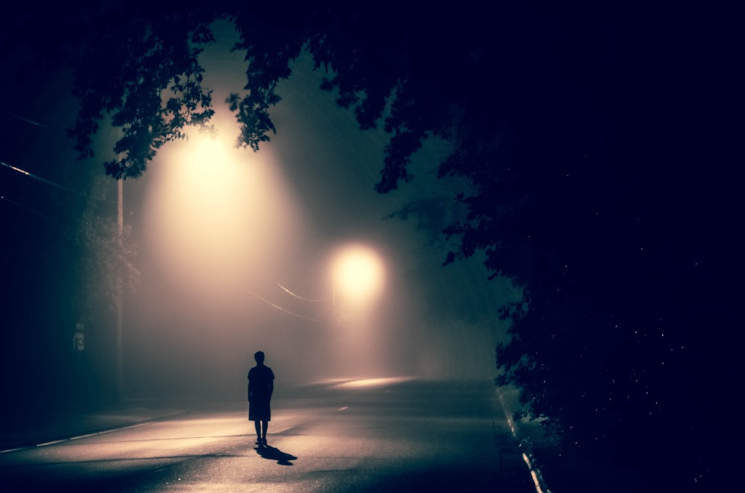 Photo by Atharva Tulsi silhouette of person standing on concrete road with streetlights turned on during nighttime